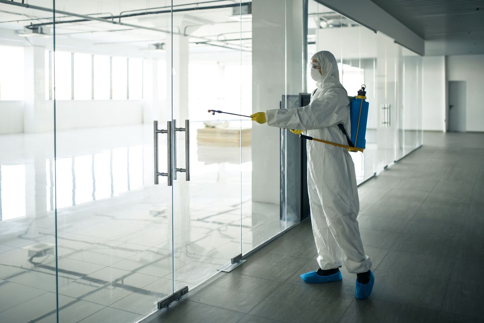 Technician in a protective suit spraying disinfectant on a glass door