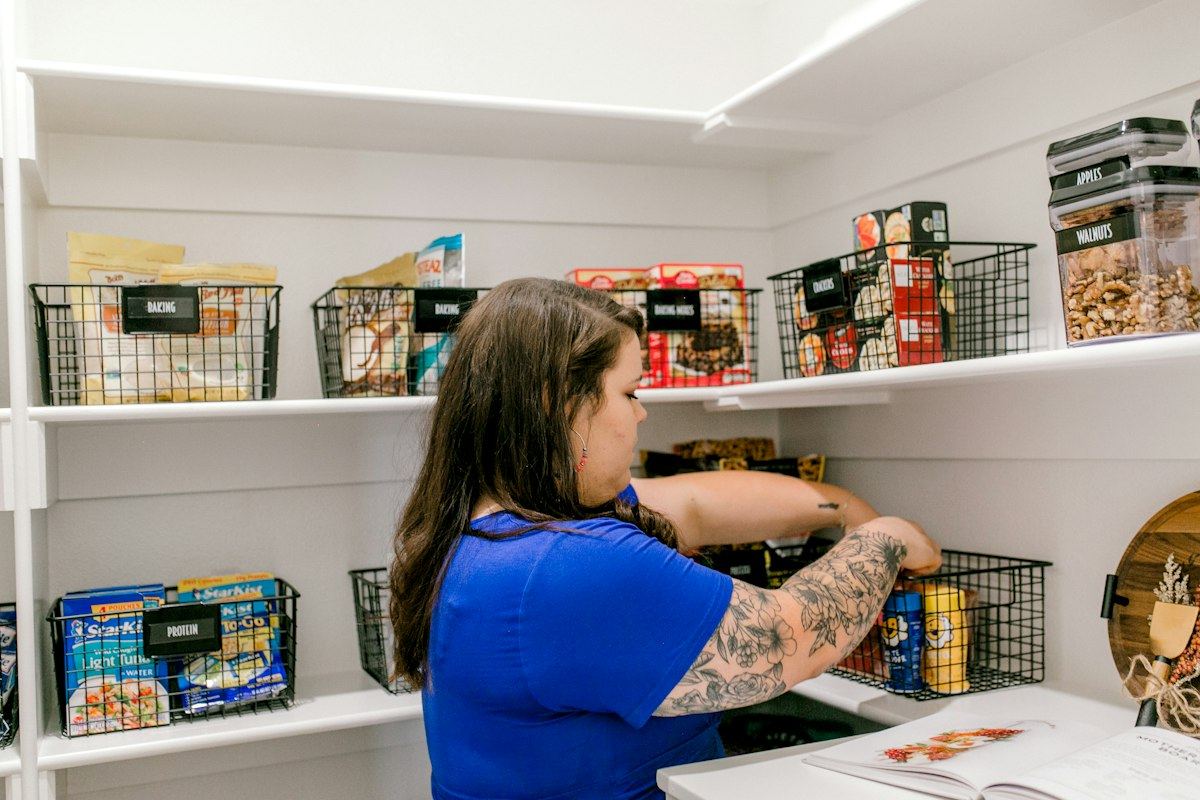 Organizer arranging food into labeled wire baskets in a white pantry