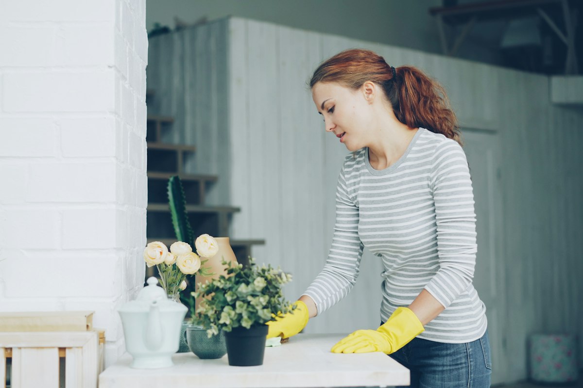 Housekeeper in yellow gloves wiping down a dining table during a regular house cleaning