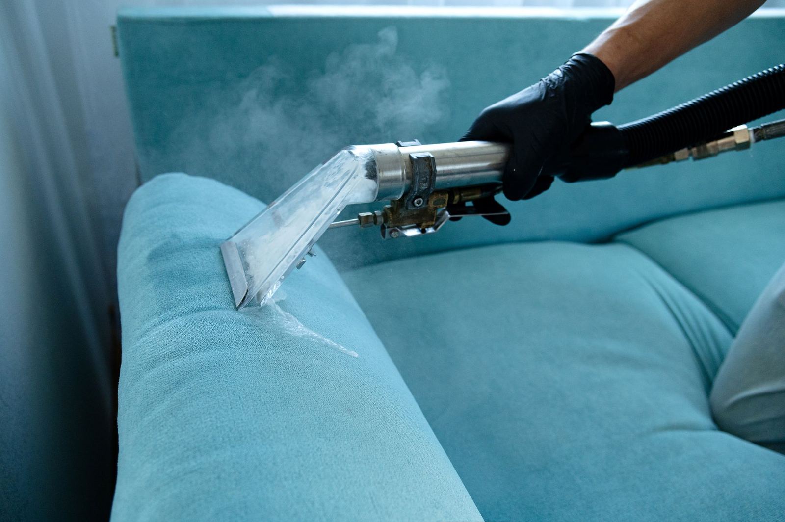 Cleaner vacuuming a blue sofa cushion during a deep house cleaning